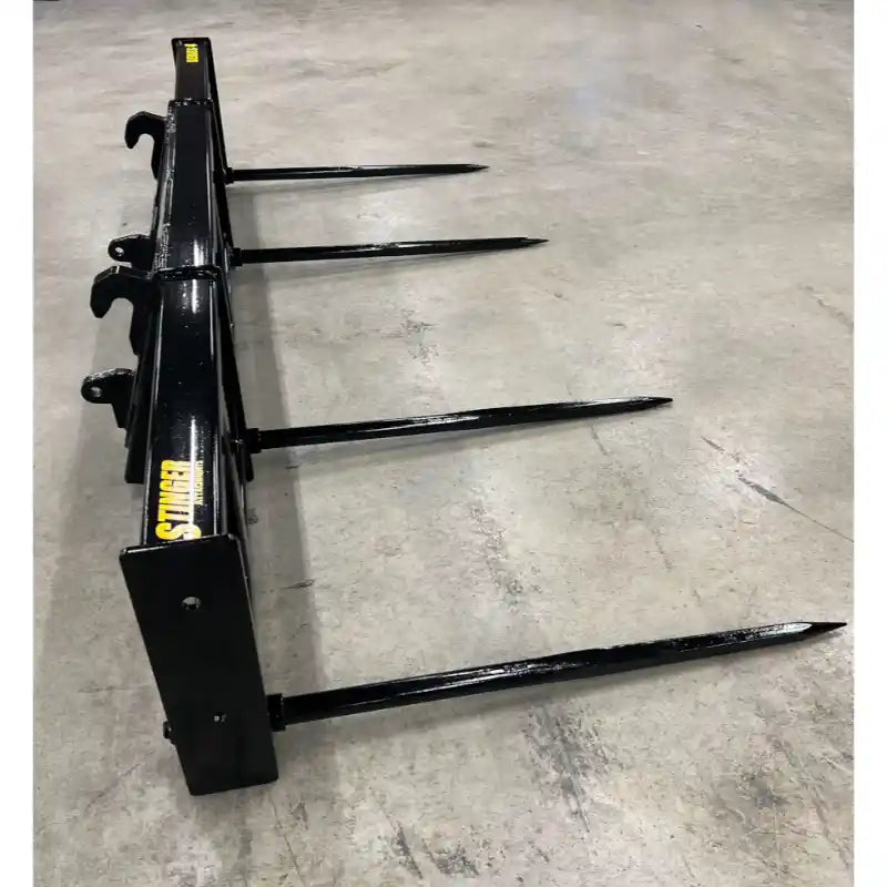Heavy-duty black metal bale spear attachment with four long pointed spears on concrete floor