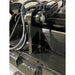 Close-up of black steel grapple bucket hinge with hydraulic hoses and mounting bracket on indoor concrete floor