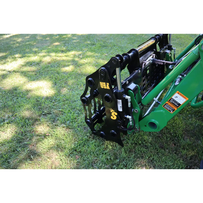 Black steel mechanical grapple attachment connected to green loader arm, positioned closed over grass outdoors