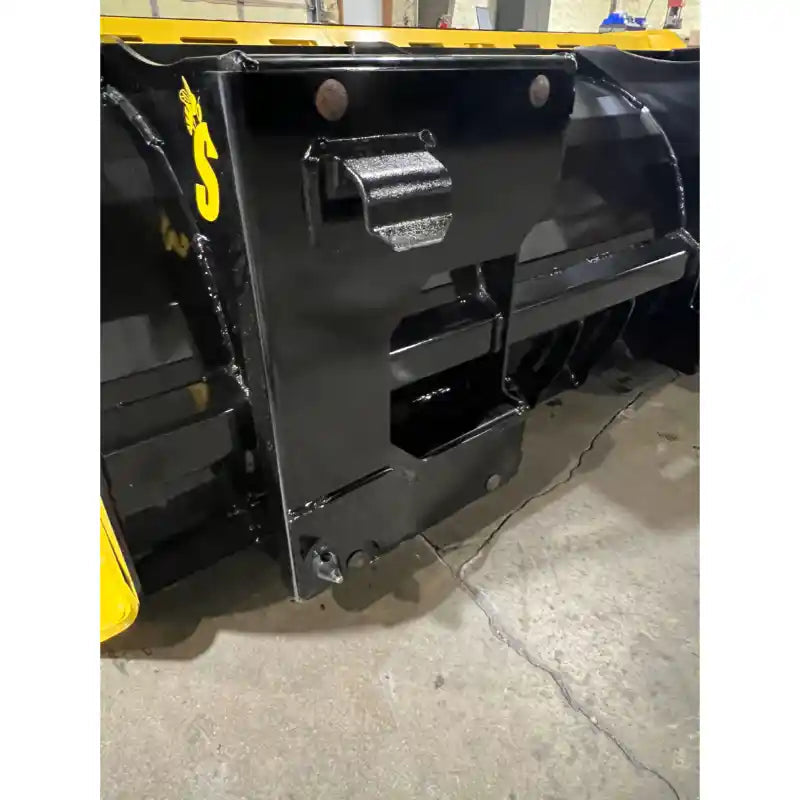 Close-up of black steel mounting bracket on yellow and black snow pusher attachment on concrete floor indoors