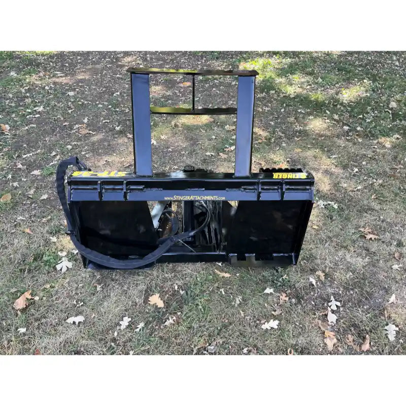 Black steel tractor-mounted tree puller attachment with reinforced frame and hydraulic hose on grass terrain