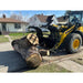 Yellow Komatsu loader with black hydraulic grapple attachment lifting large tree log on residential street