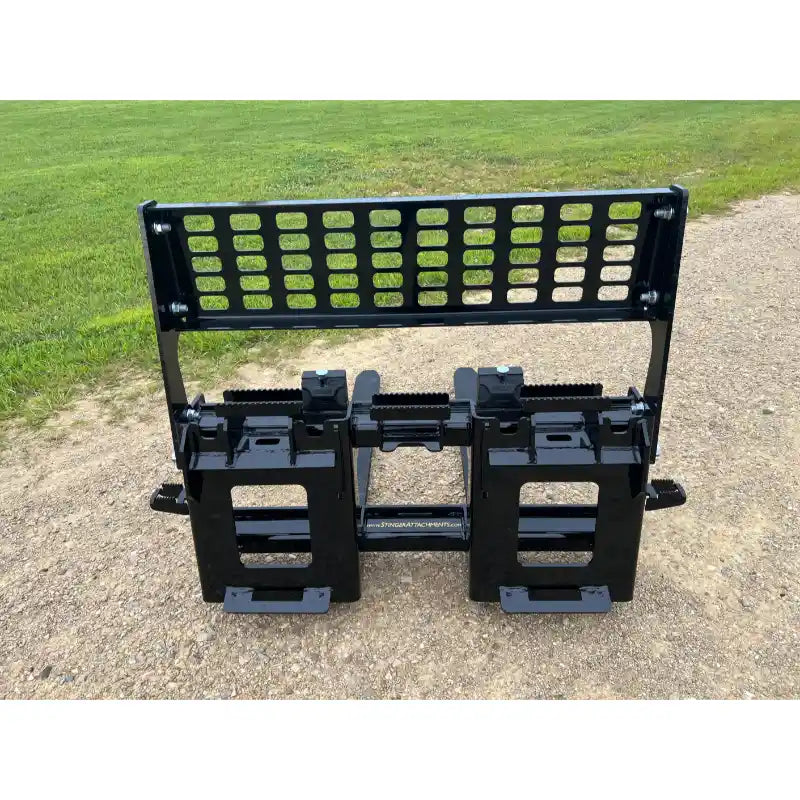 Black steel skid steer pallet fork carriage plate with perforated backrest and adjustable fork locks on gravel surface