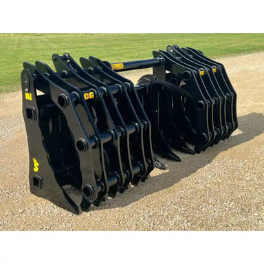 Two large black steel clam grapple attachments with reinforced frames and multiple heavy tines resting on gravel outdoors