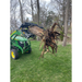 Green compact tractor with black steel grapple attachment lifting a large tree stump with exposed roots on grass outdoors