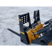 Black painted steel skid steer pallet forks attachment with reinforced backrest and two fork tines on dirt surface