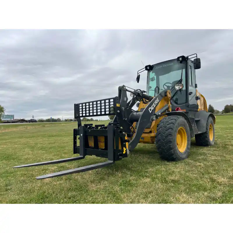 Yellow and black loader with skid steer pallet fork attachment on grass under cloudy sky