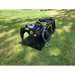 Skid steer rock grapple attachment with black metal frame, curved tines, hydraulic cylinders, and hoses on grass surface