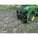 Green tractor with black steel pallet fork attachment featuring open grid backrest and extended fork tines on grass and dirt ground