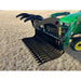 Black steel rock grapple attachment with serrated curved tines mounted on green tractor loader arm over dry grass