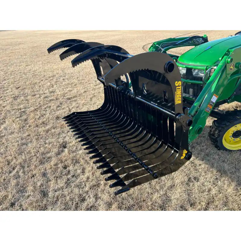 Black steel rock grapple attachment with serrated curved tines mounted on green tractor loader arm over dry grass