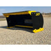 Front-left view of black and yellow skid steer snow pusher attachment resting on gravel outdoors