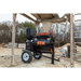 Tow-behind mortar mixer with black mixing drum, orange safety grate, and pneumatic tire on construction site dirt ground