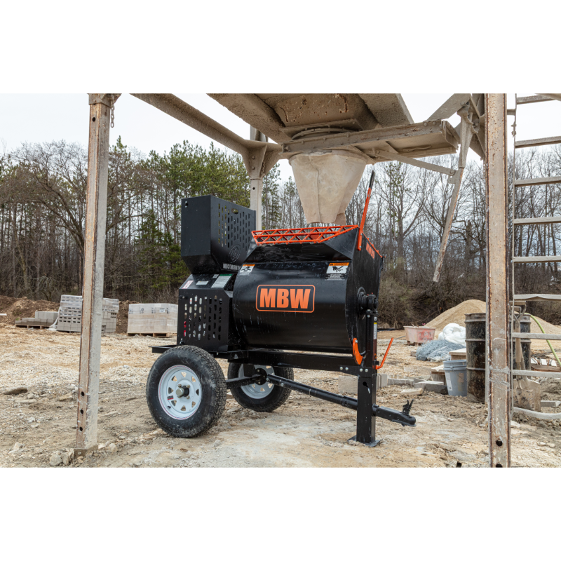 Tow-behind mortar mixer with black mixing drum, orange safety grate, and pneumatic tire on construction site dirt ground