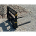 Black steel skid steer pallet fork attachment with reinforced grid backrest and two horizontal forks on gravel ground