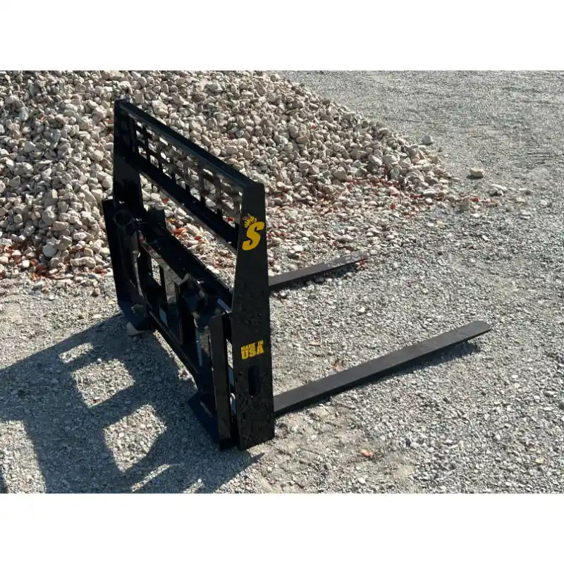 Black steel skid steer pallet fork attachment with reinforced grid backrest and two horizontal forks on gravel ground