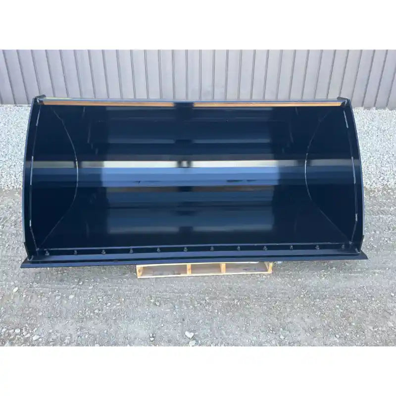 Overhead view of black steel skid steer construction bucket with bolt-on cutting edge on gravel surface