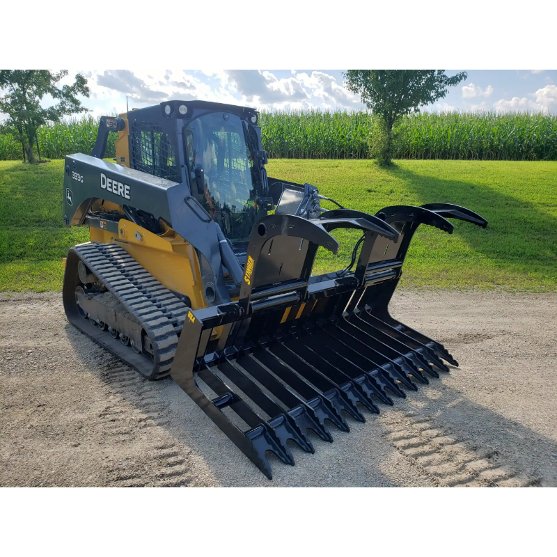 Compact track loader with black grapple attachment featuring serrated tines and dual curved arms on dirt surface outdoors
