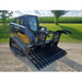 Yellow and black skid steer with a black grapple attachment featuring wide curved tines and reinforced teeth on dirt surface