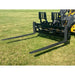 Black steel skid steer pallet forks with perforated backrest and two extended tines attached to yellow loader arm on grass