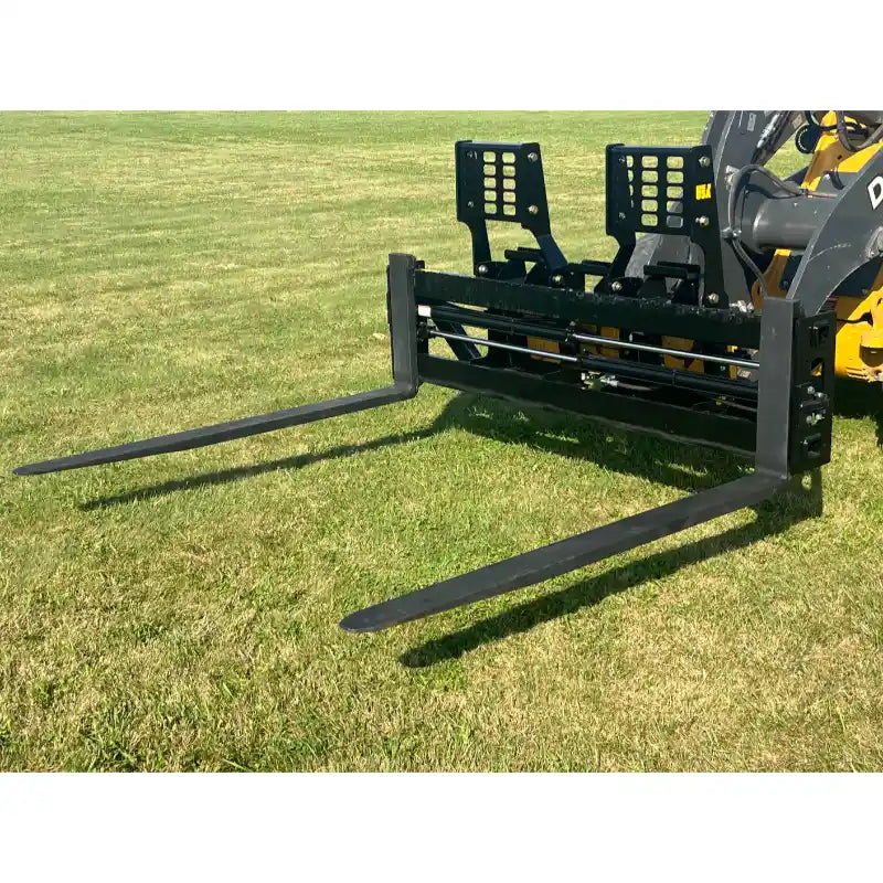 Black steel skid steer pallet forks with perforated backrest and two extended tines attached to yellow loader arm on grass