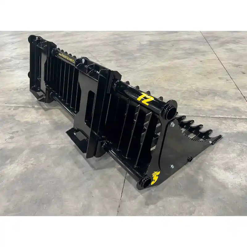 Black steel skid steer rock bucket attachment with wide spaced flat tines and reinforced mounting points on concrete floor