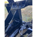 Close-up of black steel hinge and reinforced mounting bracket on heavy equipment attachment resting outdoors on grass