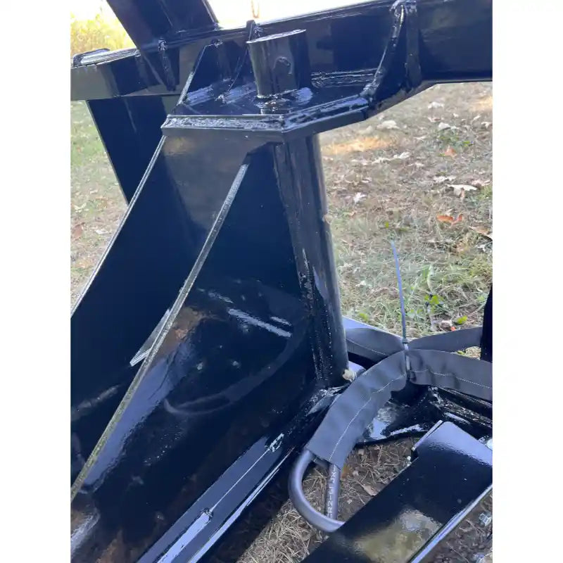 Close-up of black steel hinge and reinforced mounting bracket on heavy equipment attachment resting outdoors on grass