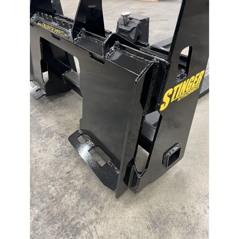 Black painted steel skid steer attachment plate with reinforced welds and yellow Stinger Attachments logo on concrete floor