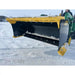 Yellow and black steel snow pusher attachment mounted on green compact loader clearing snow on paved surface