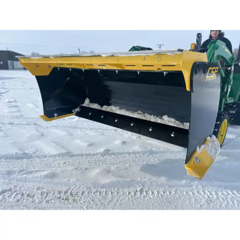 Yellow and black steel snow pusher attachment mounted on green compact loader clearing snow on paved surface