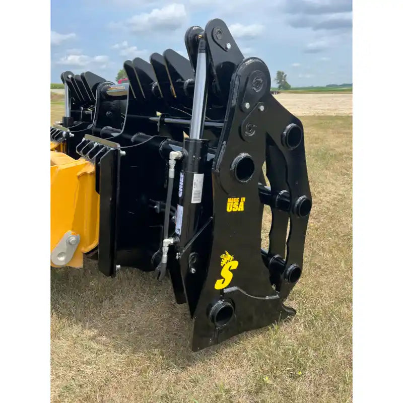 Close-up of black hydraulic loader clam-style grapple attachment with visible cylinder and latch on grassy field