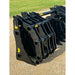 Black steel clam grapple attachment with multiple curved tines and hydraulic linkage resting on gravel outdoors
