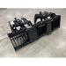 Black steel skid steer grapple attachment with dual curved arms, hydraulic cylinders, and wide spaced tines on concrete floor