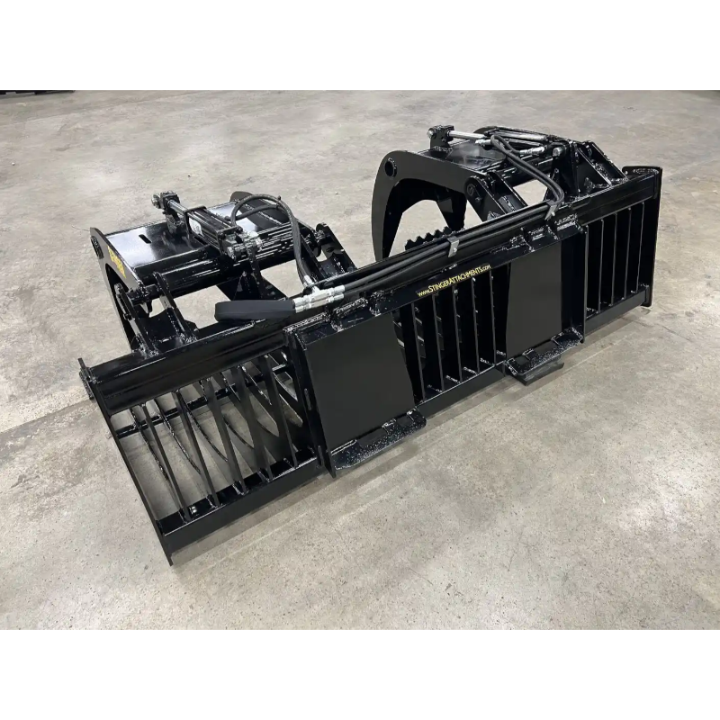 Black steel skid steer grapple attachment with dual curved arms, hydraulic cylinders, and wide spaced tines on concrete floor