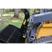 Side view of black metal skid steer rock grapple attachment with hydraulic hoses and yellow lettering on loader arm outdoors