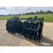 Pair of black steel clam grapple attachments with multiple curved tines and reinforced crossbars on gravel outdoors