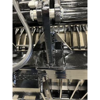 Close-up of black-painted steel hinge bracket with heavy welds and pin on skid steer rock grapple attachment