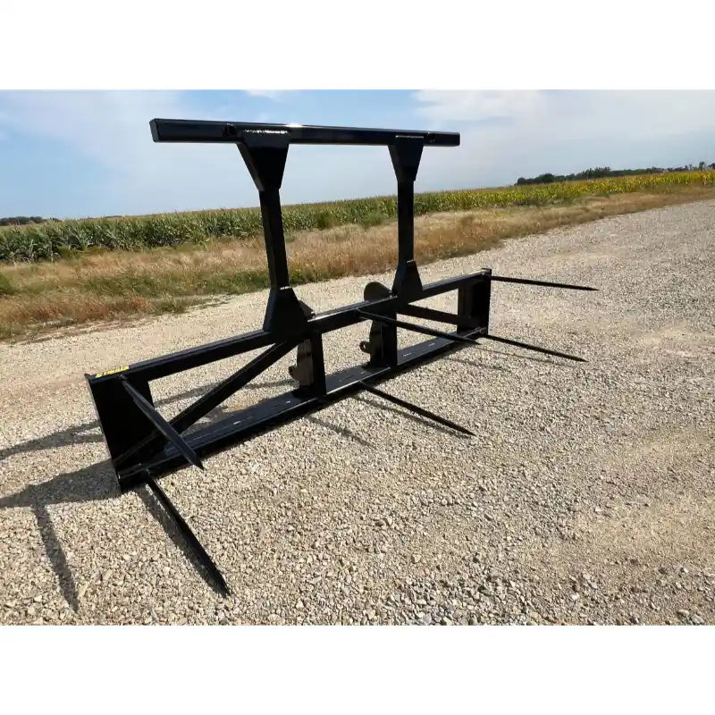 Black steel loader attachment with five pointed bale spears and reinforced frame on gravel surface outdoors