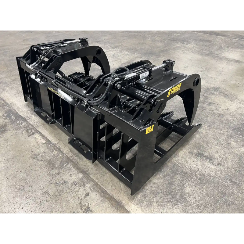 Black skid steer grapple attachment with hydraulic arms, curved tines, and reinforced steel frame on concrete floor