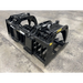 Black steel skid steer grapple attachment with dual hydraulic cylinders, curved arms, and reinforced tine bars on concrete floor