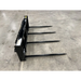 Black metal bale spear attachment with four long pointed tines on a concrete floor
