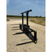 Black steel loader attachment with five long pointed bale spears and reinforced upright supports on gravel surface outdoors