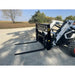 Compact black steel pallet fork attachment with perforated backrest mounted on white skid steer outdoors on gravel surface