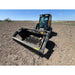 Front view of skid steer with rock bucket reel attachment on dry soil under clear blue sky