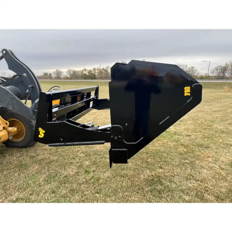 Black steel hydraulic tractor dump bucket attachment tilted outward on grassy field with visible yellow markings