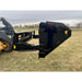 Black hydraulic tipping bucket attachment mounted on loader arm over grassy field under cloudy sky