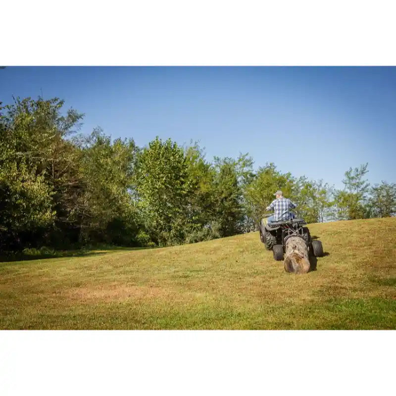 Rear view of person driving Swisher ATV Log Skidder carrying large log across grassy field, gallery position 1