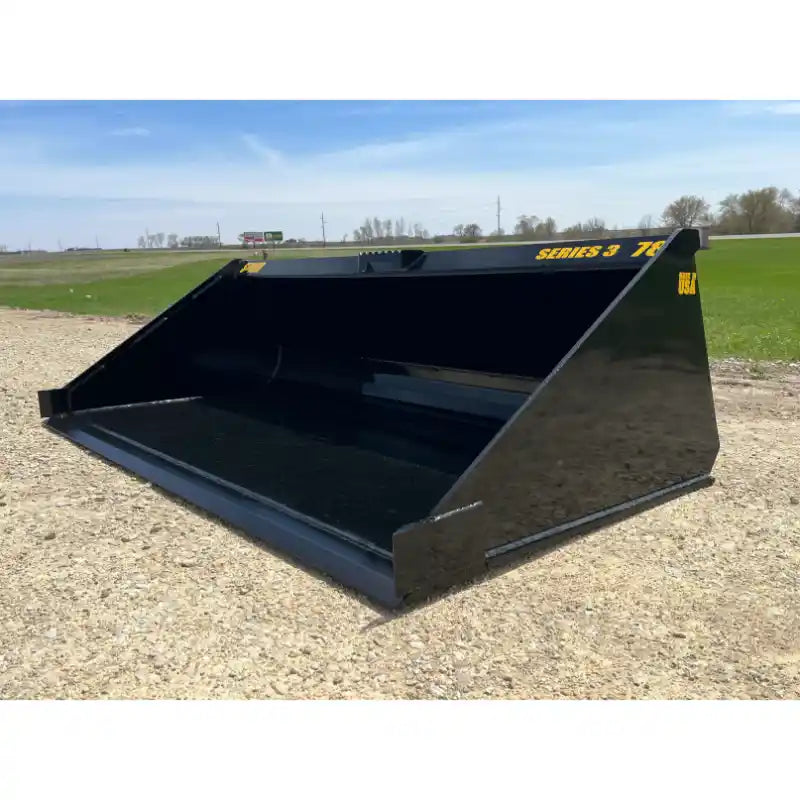 Black skid steer material bucket with smooth interior and yellow Series 3 78 decal on gravel and grass background