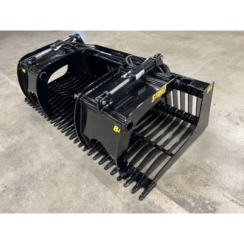 Black painted steel skid steer rock grapple attachment with twin hydraulic cylinders and spaced curved tines on concrete floor